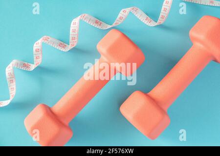 Dumbbells and measuring tape on blue background. Fitness, sport and workout concept flat lay. Weights layout Stock Photo