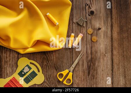 Sewing accessories and yellow fabric on wooden table. Sewing threads, needles, pins, buttons and scissors. Top view, flat lay concept. Accessories Stock Photo