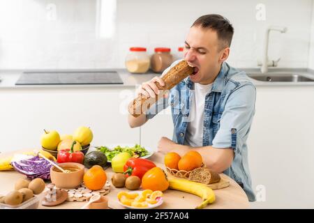 Happy young man preparing romantic dinner searching vegetable recipes diet menu, smiling husband cooking healthy vegan food cut salad in kitchen Stock Photo