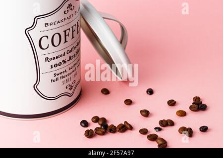 Coffee beans out of coffee pot with pot lid next to it on pink background. Stock Photo