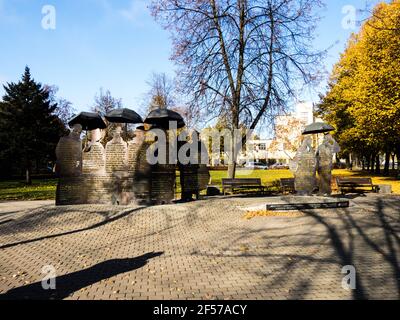 Autumn colored bushes with bright leaves and wooden bench in a city park. White flowers on foreground. Stock Photo