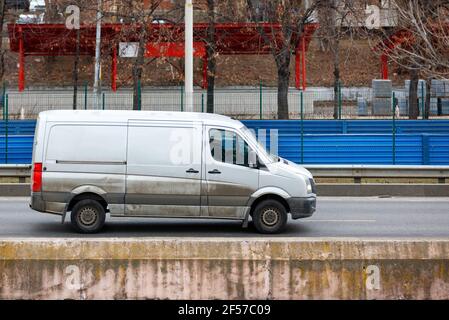 A white cargo van with muddy lower sides moves along a city street highway on a spring afternoon. Stock Photo