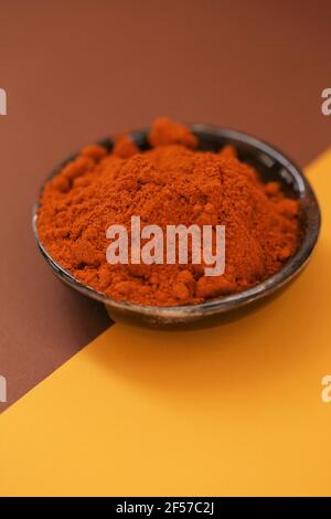 Red pepper powder.Hot pepper. Spices and condiments.Red peppers in a black ceramic plate on a brown and yellow combined background.Food and cooking Stock Photo