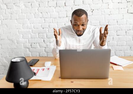 Excited african american business man is looking at the laptop screen, smiling, reading good news. Overjoyed male freelancer or student well done with Stock Photo