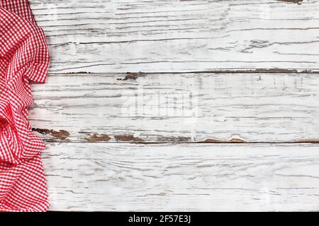 Top view of an empty white wooden picnic table and crumpled red and white gingham tablecloth at the edge of the border. Free space for text. Stock Photo