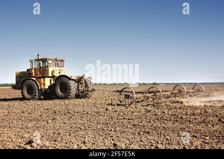 Big yellow tractor equipped with harrow working on the field. Stock Photo