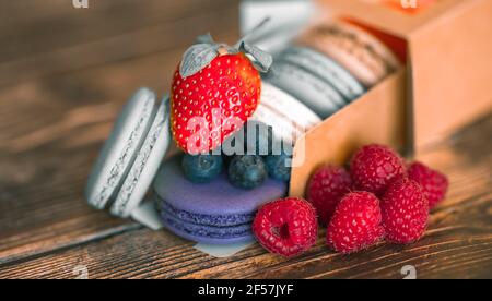 Blueberries, raspberries with strawberries on colored macaroons in a cardboard box on a wooden background Stock Photo