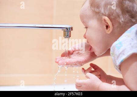 The child drinks running water from the tap. Copy space. Stock Photo