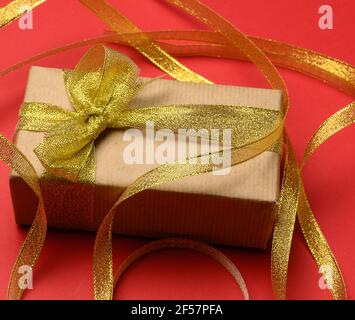 rectangular brown cardboard box tied with a silk ribbon on a red background, top view, close up Stock Photo