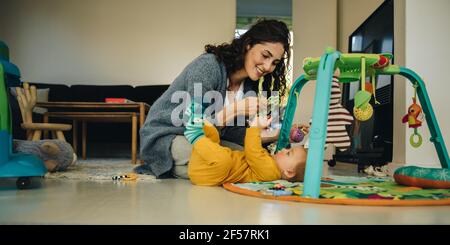 Mother using rattle toys while playing with her baby boy. Woman playing with her new born son at home. Stock Photo