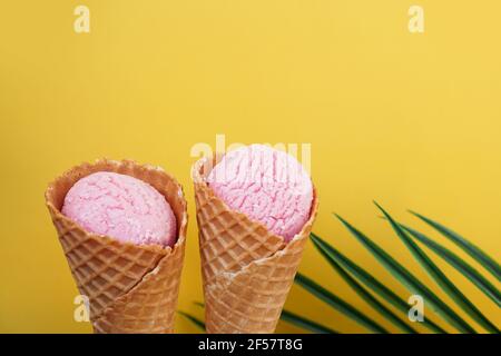Two strawberry ice creams in a cone on a yellow background. Tropical leaf Stock Photo