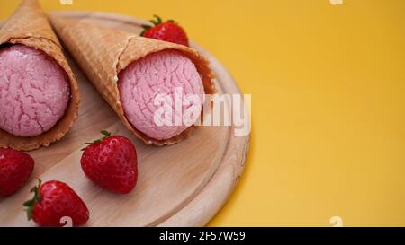Strawberry ice cream in a waffle cone. Ice cream and berries on a yellow Stock Photo