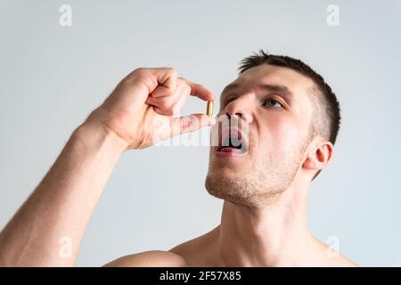 Fish oil is eaten by a man in the hands of vials and a glass bottle fish health vitamin, omega pharmacy tablet yellow closeup. People white eat female Stock Photo