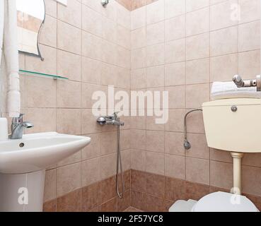 Closeup of simple style interior of small restroom with beige ceramic tile walls, white sink, classic WC toilet Stock Photo