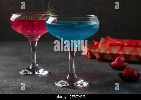 Two glasses of shimmering pink and blue champagne and heart-shaped candies on a dark background. Romantic dinner for a couple. Stock Photo