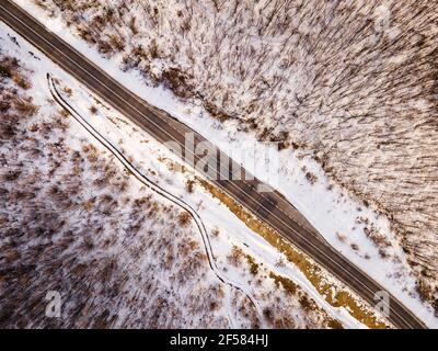 High angle top down aerial view drone image on road trough the trees and forest in mountain range covered with white snow in winter day near Knjazevac Stock Photo