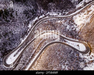 High angle aerial view drone image on the curved serpentine road trough the trees and forest in mountain range with white snow in winter day near Knja Stock Photo