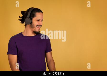 Young man smiling and listening music using headphones. Yellow background. Stock Photo