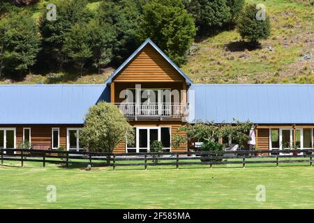 Large sunny wooden house with lot of windows and French doors in rural setting with slope behind it. Stock Photo