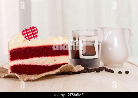 Slice of  Red velvet cake  and hot black coffee drip on the wooden table with white curtain background. Stock Photo