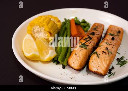 Two Pieces Salmon Steak With Vegetables Grilled Corn Asparagus Carrots Green Peas Lemon Pepper On Black Background Stock Photo Alamy