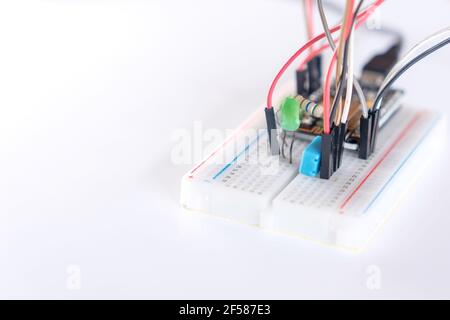 Electronic devices, LEDs, resistors, and microcontrollers on an experimental board to study Internet of Things IoT projects on white background. Stock Photo
