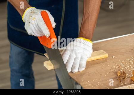 Man saws a piece of wood with a hand saw on work table. Stock Photo