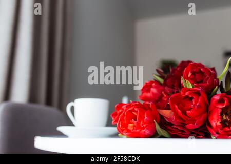 Red tulips bouquete on table, white coffee cup. Concept for greeting card for mothers day, international womans day or valentines day concept, birthda Stock Photo