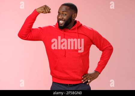 Charming cheeky friendly african-american strong guy smiling broadly proudly showing biceps raise one hand bragging muscles attend gym recommend you Stock Photo