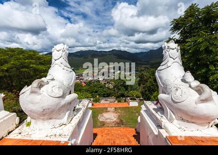 Back view of white lion statue at Wat Phra That Doi Kong Mu with aerial city view of Mae Hong Son in the mist, Thailand Stock Photo