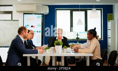 Business people comming in conference room ready for morning meeting. Mature project leader discussing with teamworkers in broadroom, analysing charts, graphs, financial evolution of company Stock Photo