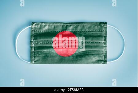 Covid-19 Coronavirus protection concept: Medical disposable face mask with Bangladesh flag on blue background. WHO recommends usage of mask for safety. Stock Photo