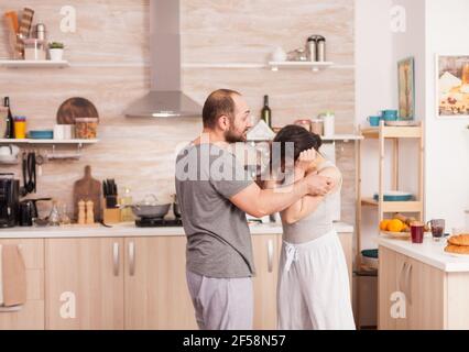 Married couple arguing at the kitchen during breakfast. Domestic violence threatening aggressive angry frustrated husband abusing physical depressed sad unhappy crying stressed woman. Home abuse Stock Photo