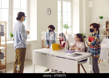 Tutor teaching pupils small group in classroom, people in face mask shot Stock Photo