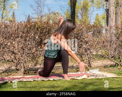 Young Caucasian brunette lady doing yoga in a park on a sunny day wearing a sanitary mask Stock Photo