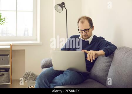 Serious mature man studying working on laptop sitting on couch at home Stock Photo