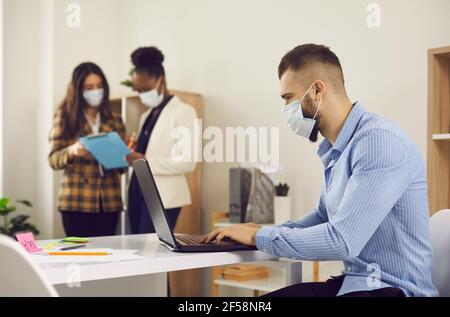 Man employee in face medical mask working on laptop in office after lockdown Stock Photo