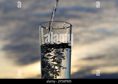Clean water pouring into drinking glass on sunset blurred background. Concept of health and freshness, thirst, water purification Stock Photo