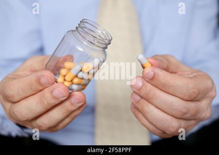 Man in office clothes taking pills, bottle of medication in capsules close up. Concept of antidepressant, stress at work, vitamins, dose of drugs Stock Photo