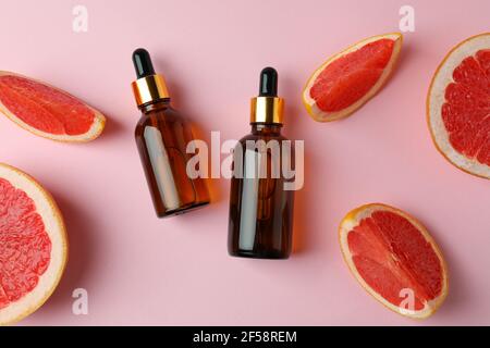 Dropper bottles with oil and grapefruit slices on pink background Stock Photo