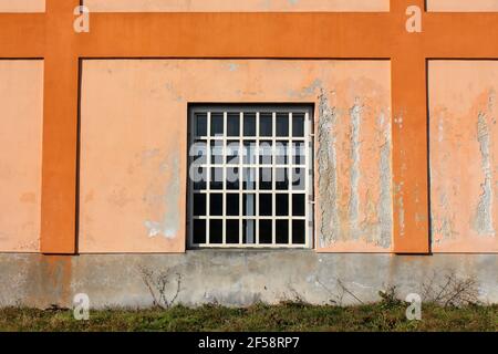 New window with white plastic frame and metal bars protection mounted on colorful old dilapidated industrial factory building wall with cracked facade Stock Photo