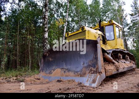 Dozer during clearing forest for construction new road . Yellow Bulldozer at forestry work Earth-moving equipment at road work, land clearing, grading Stock Photo