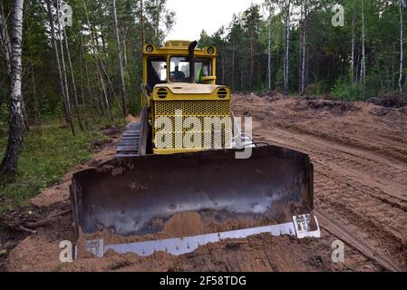 Dozer during clearing forest for construction new road . Yellow Bulldozer at forestry work Earth-moving equipment at road work, land clearing, grading Stock Photo