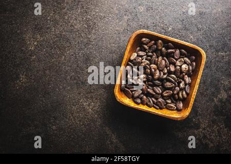 Roasted cocoa beans in wooden bowl on black table. Top view. Stock Photo