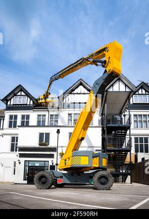 Yellow mechanical elevated working platform hydraulic boom arm extended to work at height MEWP. Cherry picker extended raised high up in air repairs Stock Photo