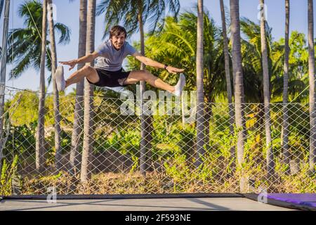 Happy man jumping on an outdoor trampoline, against the backdrop of palm trees Stock Photo