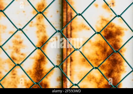 Mesh pattern on the background of a rusty iron wall. Green chain-link fence and corrosive sheet metal Stock Photo