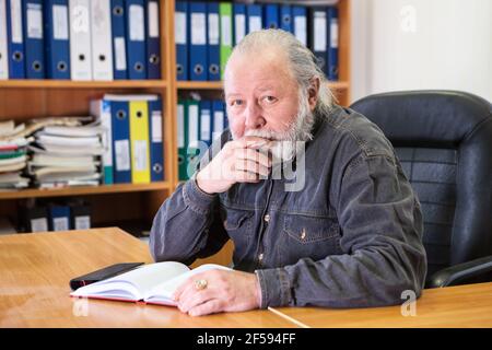 An elder man a teacher of the highest rank in a college or university. Bearded man professor sits in a leather chair in office room Stock Photo