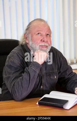 Absorbed pensive mature businessman thinking about problems with pan in hand and notebook on the table Stock Photo
