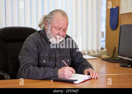 Senior businessman taking notes in notebook in his modern office Stock Photo